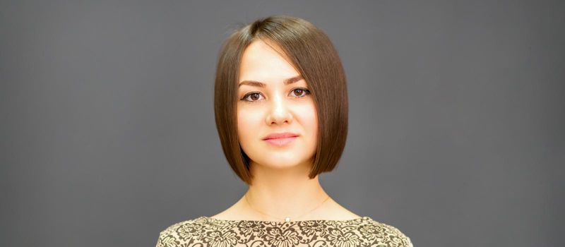 Beautiful young caucasian brunette woman with short hairstyle smiling and looking at camera against dark gray background with copy space