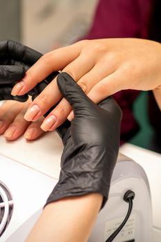 Close up professional manicure master holds the female hand of the customer and checks the manicure in a nail salon