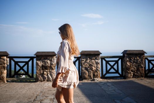 Young woman with long blond hair in a light top and skirt walks on a summer sunny day