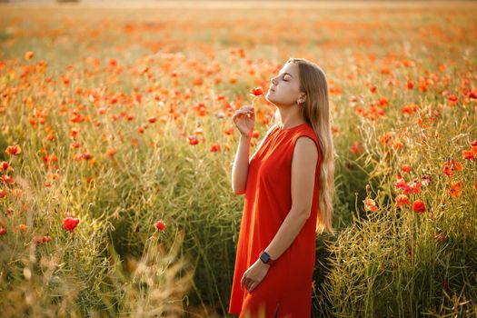 A woman of European appearance with long blonde hair and a red summer dress, she stands in a blooming poppy field