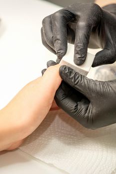 Close up of the caucasian hands of a professional manicurist are filing the nails of a young woman. Young caucasian woman receiving a manicure by a beautician with a nail file in a nail salon