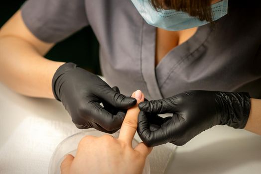 Close up professional manicure master holds the female hand of the customer and checks the manicure in a nail salon