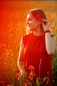 Happy blonde woman in red dress holding a flower in her hair on a poppy field. Fun summer vibes. Relaxed atmosphere, positive emotions.