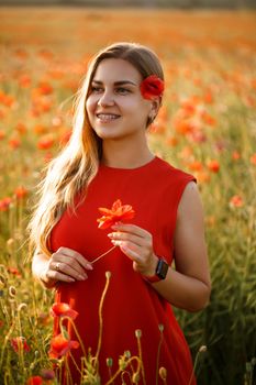Happy blonde woman in red dress holding a flower in her hair on a poppy field. Fun summer vibes. Relaxed atmosphere, positive emotions.