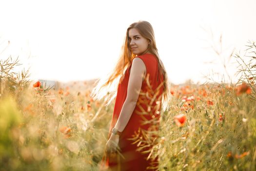 Happy blonde woman in red dress holding a flower in her hair on a poppy field. Fun summer vibes. Relaxed atmosphere, positive emotions.