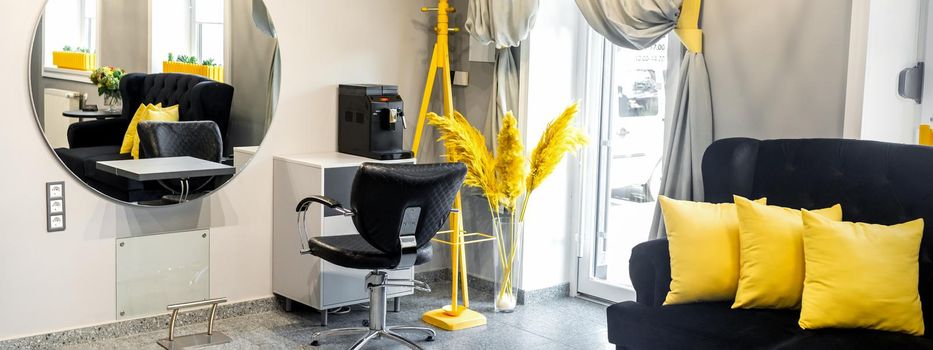 Modern small bright hair and beauty salon in black and yellow colors with gray walls and floor and black sofa with yellow cushions