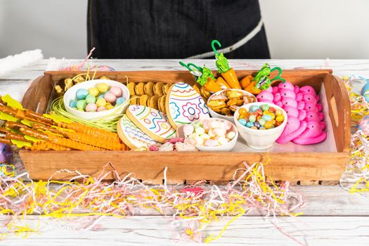 Assembling charcuterie board with Easter candies, cookies, and marshmallows.