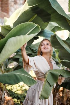 Beautiful woman in the jungle. A resort or hotel with tropical trees and plants. Woman with near banana leaf. Girl on vacation in the rainforest