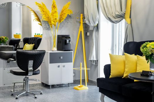 Modern small bright hair and beauty salon in black and yellow colors with gray walls and floor and black sofa with yellow cushions