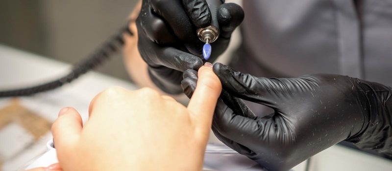 Manicure master uses electric nail file machine in a nail salon, close up