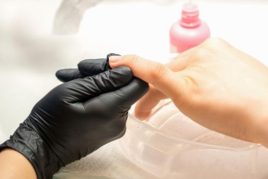 Close up professional manicure master holds the female hand of the customer and disinfects nails in a nail salon