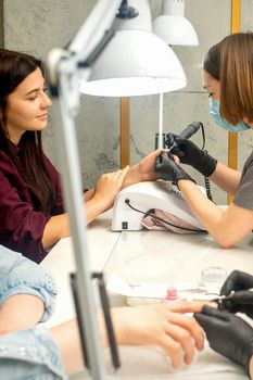Manicure master in rubber gloves applies an electric nail file to remove the nail polish in a nail salon
