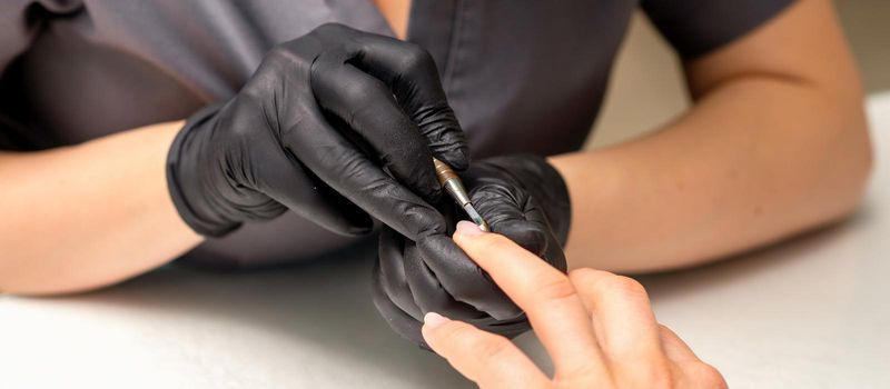 Close up professional manicurist master holding customer hand while using a cuticle pusher in a nail salon