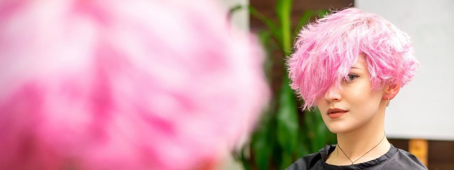 The beautiful young caucasian woman with a new pink short hairstyle in the mirror reflection looking at the camera in a hairdresser salon