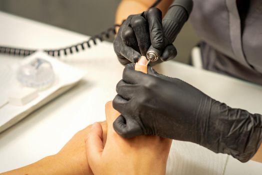 Manicure master uses electric nail file machine in a nail salon, close up