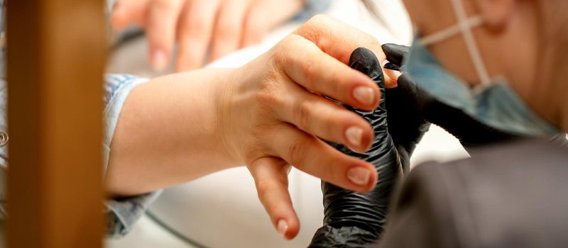 Manicure painting process. Manicure master paint the nails with transparent varnish in a nail salon, close up