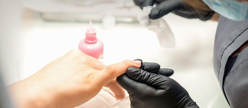 Close up professional manicure master holds the female hand of the customer and disinfects nails in a nail salon