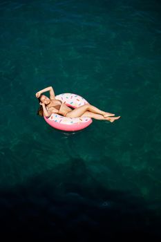 Young woman in a swimsuit swims on an inflatable ring in the sea. Summer vacation concept.