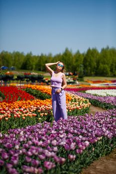 A young woman in a pink suit stands in a blooming field of tulips. Spring time