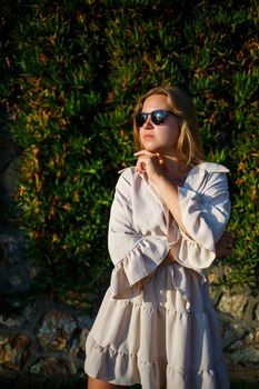 Young beautiful woman in sunglasses walks under the bright sun, she is in a beige short skirt and top