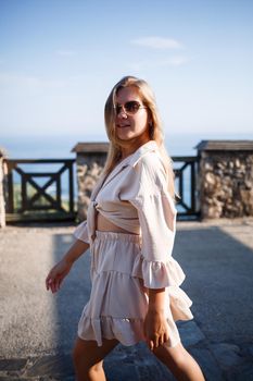 Young woman with long blond hair in a light top and skirt walks on a summer sunny day