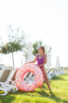 A beautiful woman holds an inflatable circle in her hands, standing on the green grass. Attractive model with perfect body. Vacation concept, the girl goes to swim in the sea