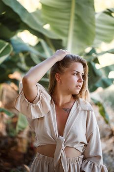 A woman stands near green banana leaves on the island. Tropical trees