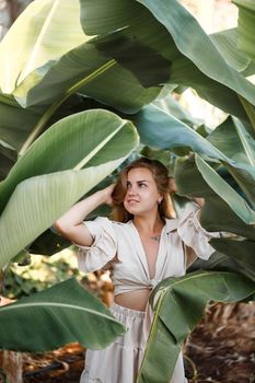 Beautiful woman in the jungle. A resort or hotel with tropical trees and plants. Woman with near banana leaf. Girl on vacation in the rainforest