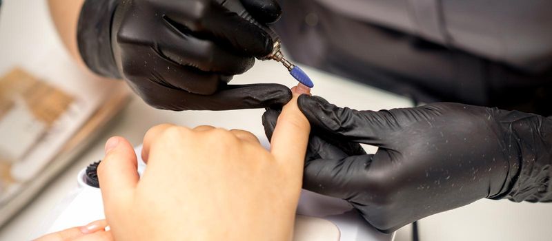 Manicure master uses electric nail file machine in a nail salon, close up