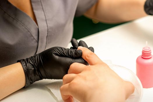 Close up professional manicure master holds the female hand of the customer and disinfects nails in a nail salon