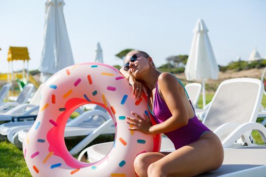 Happy young woman in stylish sunglasses and swimsuit with inflatable ring on vacation. Attractive tender girl in the sun, sunbathing and relaxing