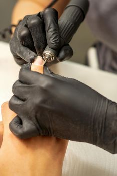 Manicure master uses electric nail file machine in a nail salon, close up