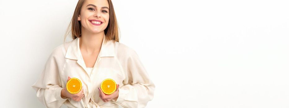 Young Caucasian smiling woman holding slices orange over isolated white background, breast health concept