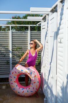 Happy young woman in stylish sunglasses and swimsuit with inflatable ring on vacation. Attractive tender girl in the sun, sunbathing and relaxing