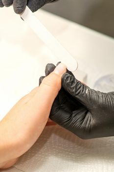 Close up of the caucasian hands of a professional manicurist are filing the nails of a young woman. Young caucasian woman receiving a manicure by a beautician with a nail file in a nail salon