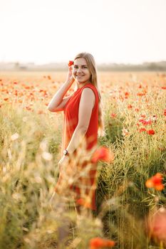 A woman of European appearance with long blonde hair and a red summer dress, she stands in a blooming poppy field