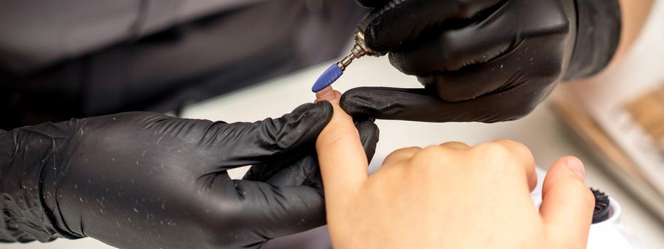 Manicure master uses electric nail file machine in a nail salon, close up