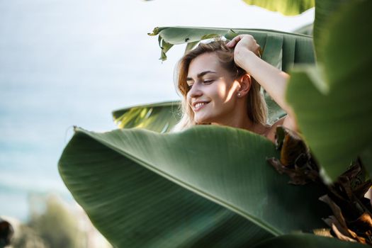 A woman stands near green banana leaves on the island. Tropical trees