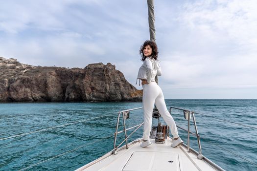 Woman standing on the nose of the yacht at a sunny summer day, breeze developing hair, beautiful sea on background.