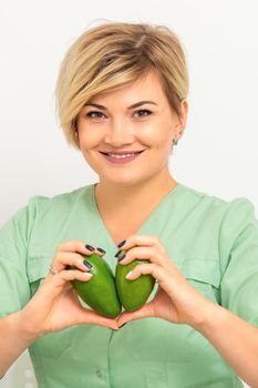 Female nutritionist doctor wearing green workwear holding green organic avocado fruit. Healthy lifestyle concept