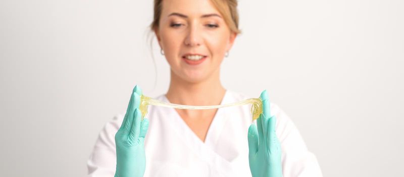 Young caucasian smiling female beautician holding wax for depilation over white background. Yellow sugar paste in hands master of depilation. Epilation concept