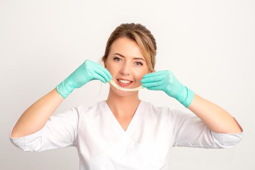 Young caucasian smiling female beautician holding wax for depilation over white background. Yellow sugar paste in hands master of depilation. Epilation concept