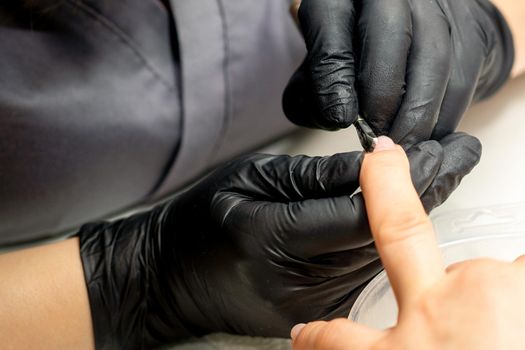 Close up professional manicurist master holding customer hand while using a cuticle pusher in a nail salon