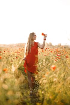 A woman of European appearance with long blonde hair and a red summer dress, she stands in a blooming poppy field
