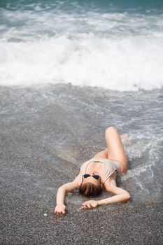 woman in beige swimsuit lies on an empty sandy beach near the ocean. Selective focus