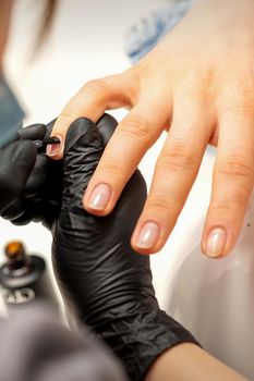 Manicure painting process. Manicure master paint the nails with transparent varnish in a nail salon, close up