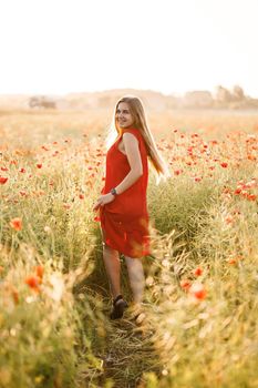 A woman of European appearance with long blonde hair and a red summer dress, she stands in a blooming poppy field