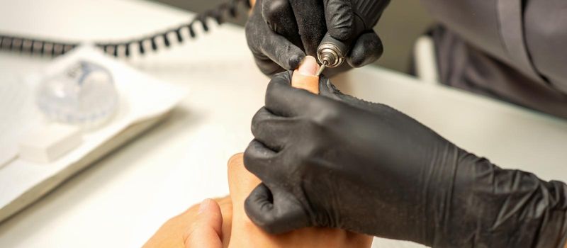 Manicure master uses electric nail file machine in a nail salon, close up