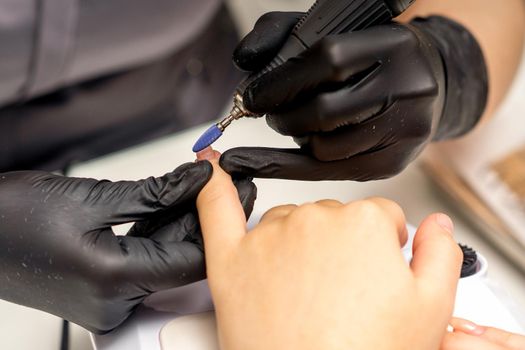 Manicure master uses electric nail file machine in a nail salon, close up