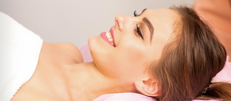 A beautiful smiling young woman is lying on a massage couch waiting for a massage in a massage room